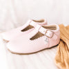 Little Love Bug Company's pink leather t-bar shoes on a white blanket.