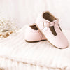 Pink t-bar leather shoes by Little Love Bug company sitting on a white blanket.