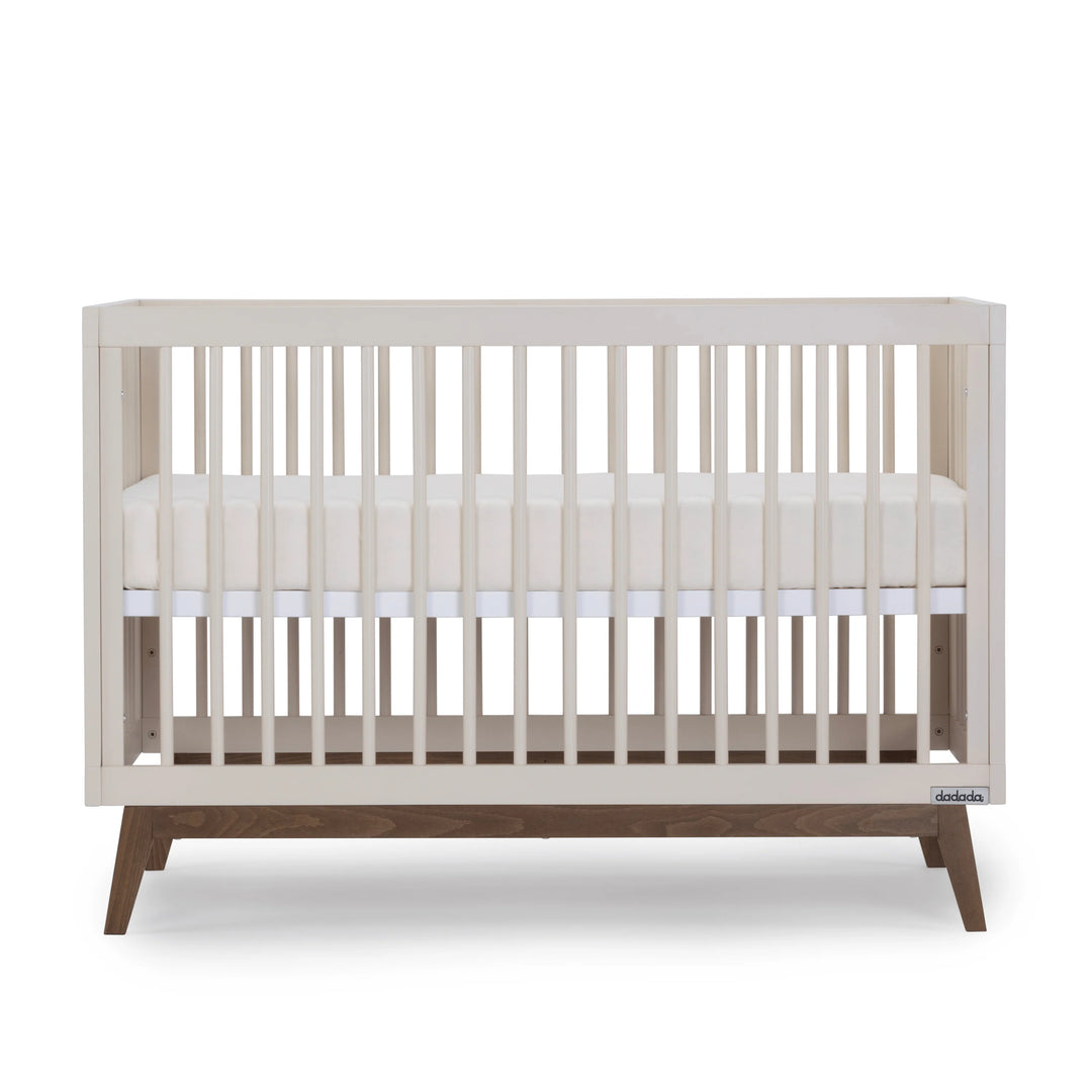 Side angle of the Dadada Soho 3-in-1 Convertible Crib in almond milk walnut displayed as a crib to toddler bed.