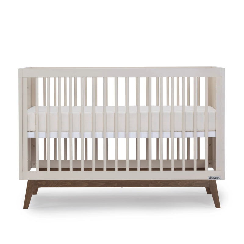 Side angle of the Dadada Soho 3-in-1 Convertible Crib in almond milk walnut displayed as a crib to toddler bed.