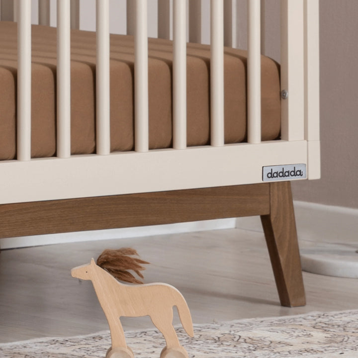 Close-up of the Dadada Soho 3-in-1 Convertible Crib in almond milk walnut finish displayed as a crib wood.