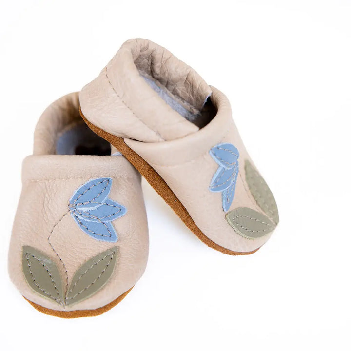 soft leather baby shoes on beige leather with blue flower motif and soft sued bottoms