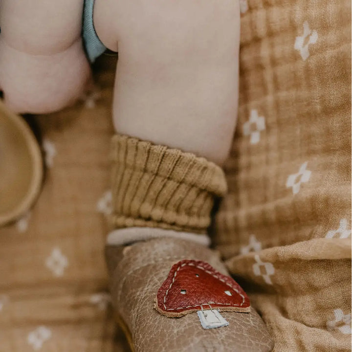 close up of a chubby baby leg wearing soft adjustable real leather brown starry knight design shoes with mushroom 