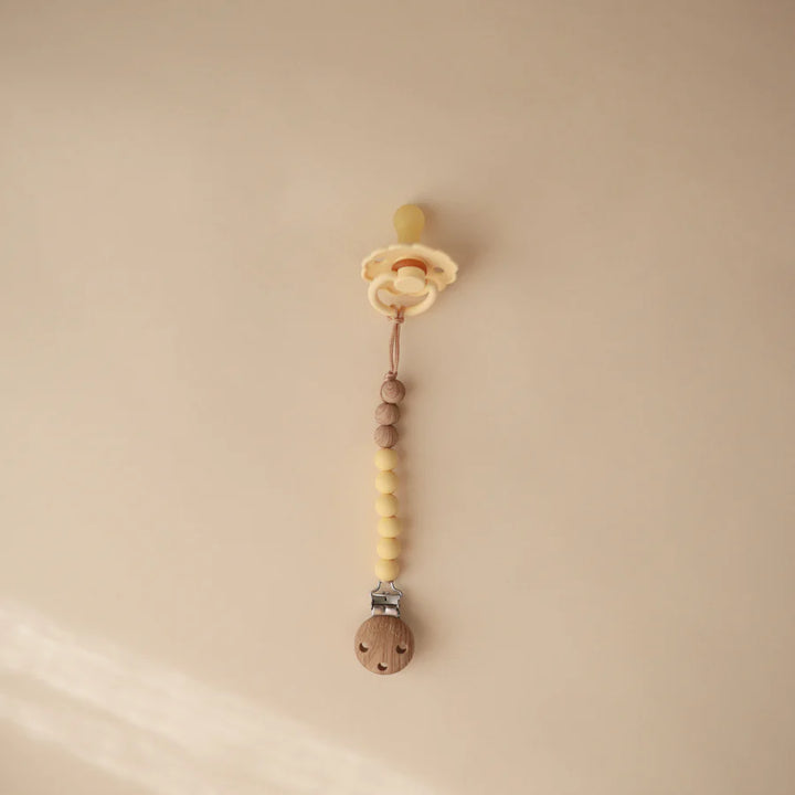 Soft silicone Mushie Eva Pacifier Clip in Mustard Yellow offers a safe and clean pacifier holder.