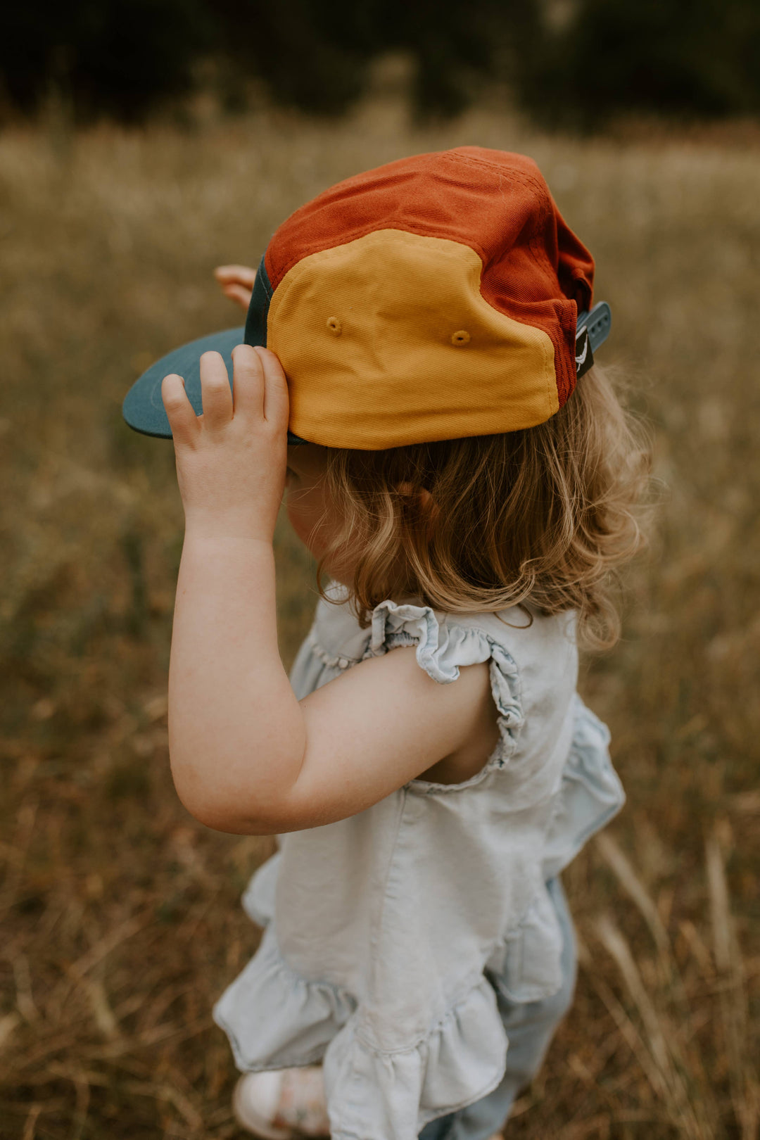 Girl in a white dress adjusts her Trek Light hat while exploring a wooded backdrop
