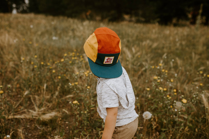 Boy strolls through a field of wildflowers wearing his Trek Light camp hat