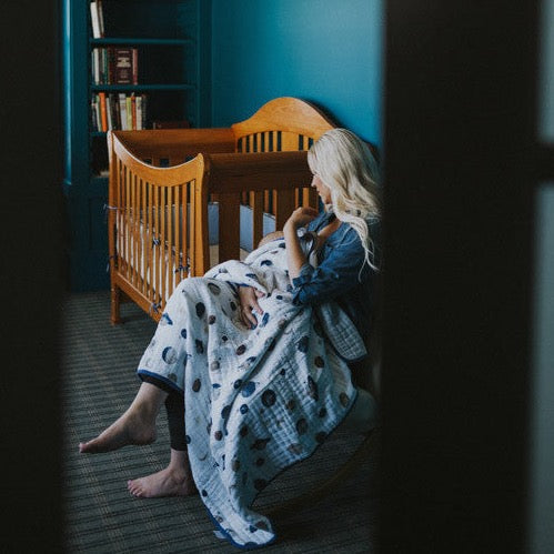 Little Unicorn Original Cotton Muslin Quilt - Planetary displayed in a nursery, a cozy baby quilt with playful outer space details.