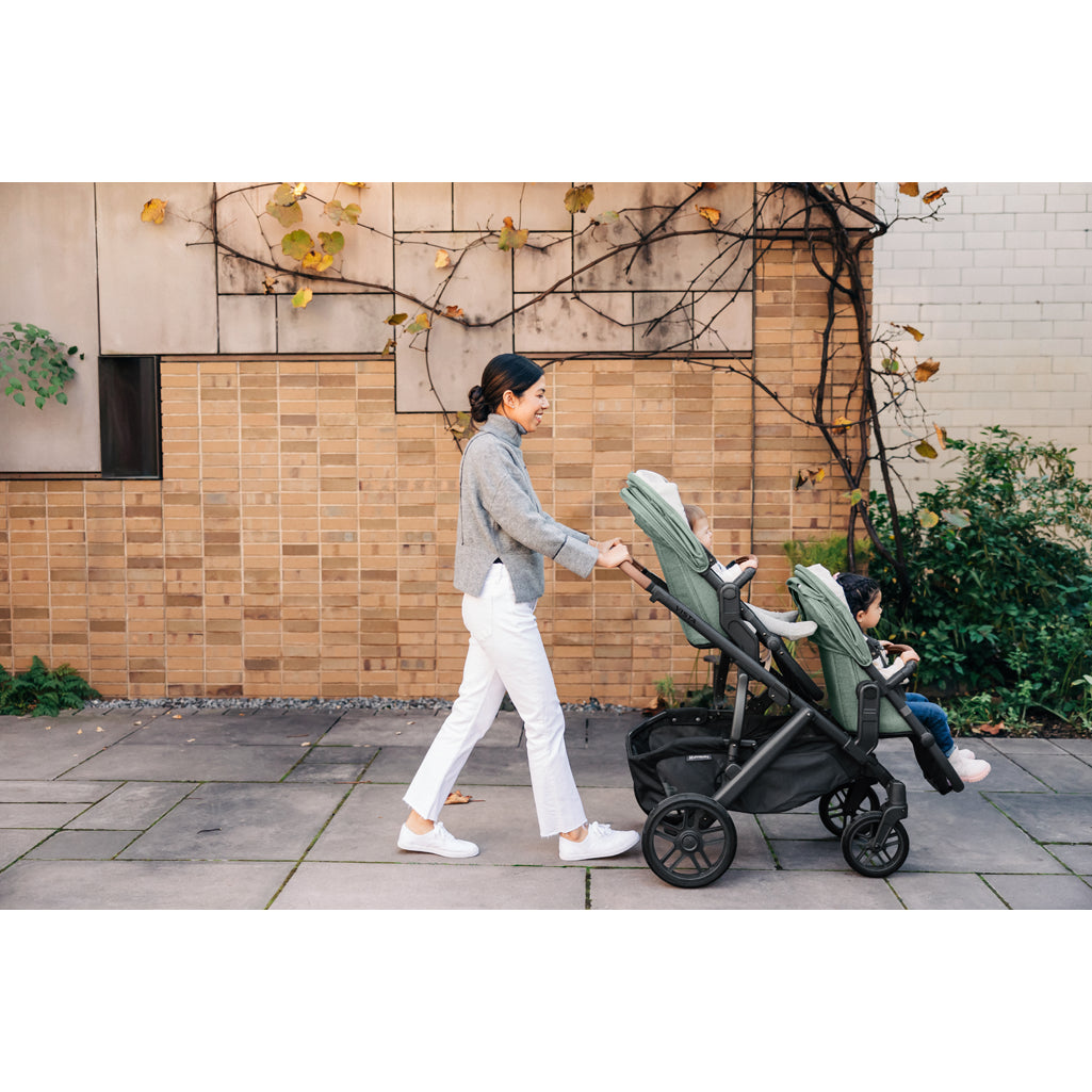 Parents pushing the UPPAbaby Vista V3 Twin Double Stroller with infant and toddler, ideal stroller travel system
