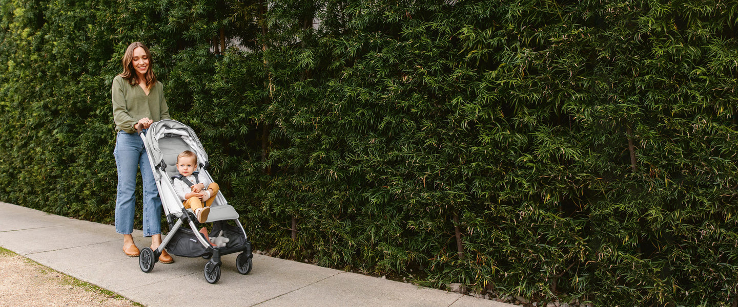 mom pushing UPPAbaby vista stroller in front of hedges
