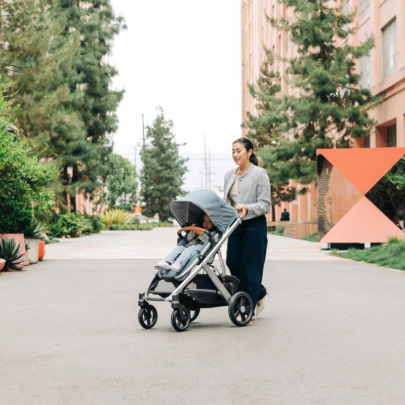 Woman pushing an UPPAbaby Vista v3 stroller with a child on a sidewalk.