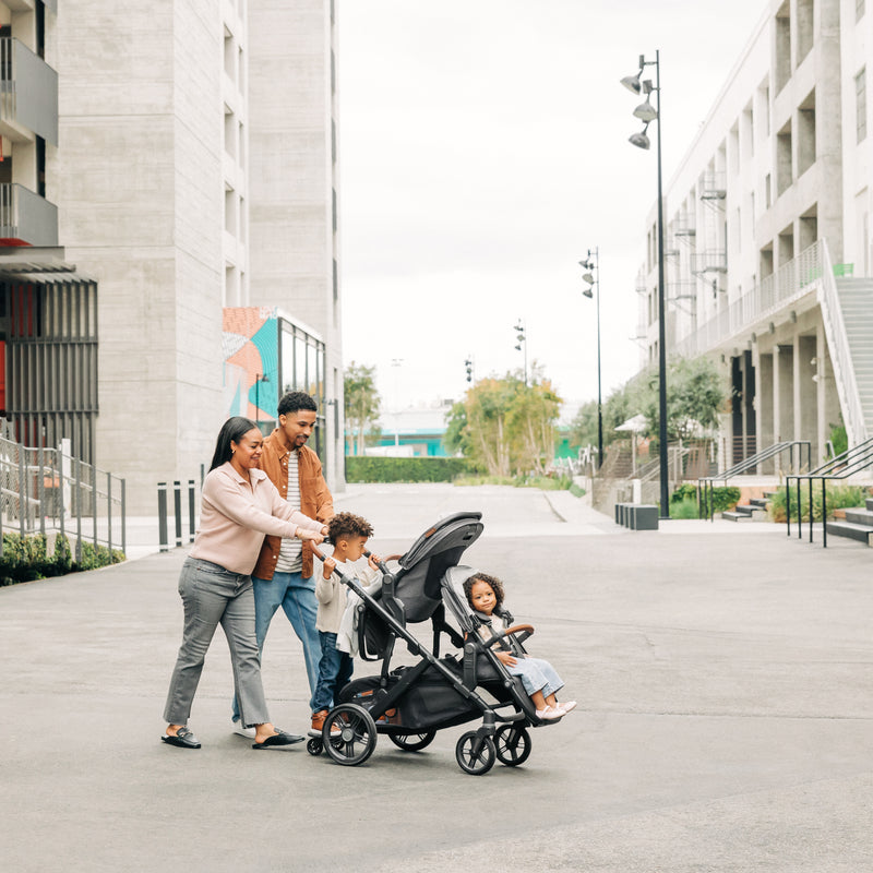 Family with a Uppababy vista v3 travel system stroller and rumbleseat v3 and piggyback rider board walking on a city street.