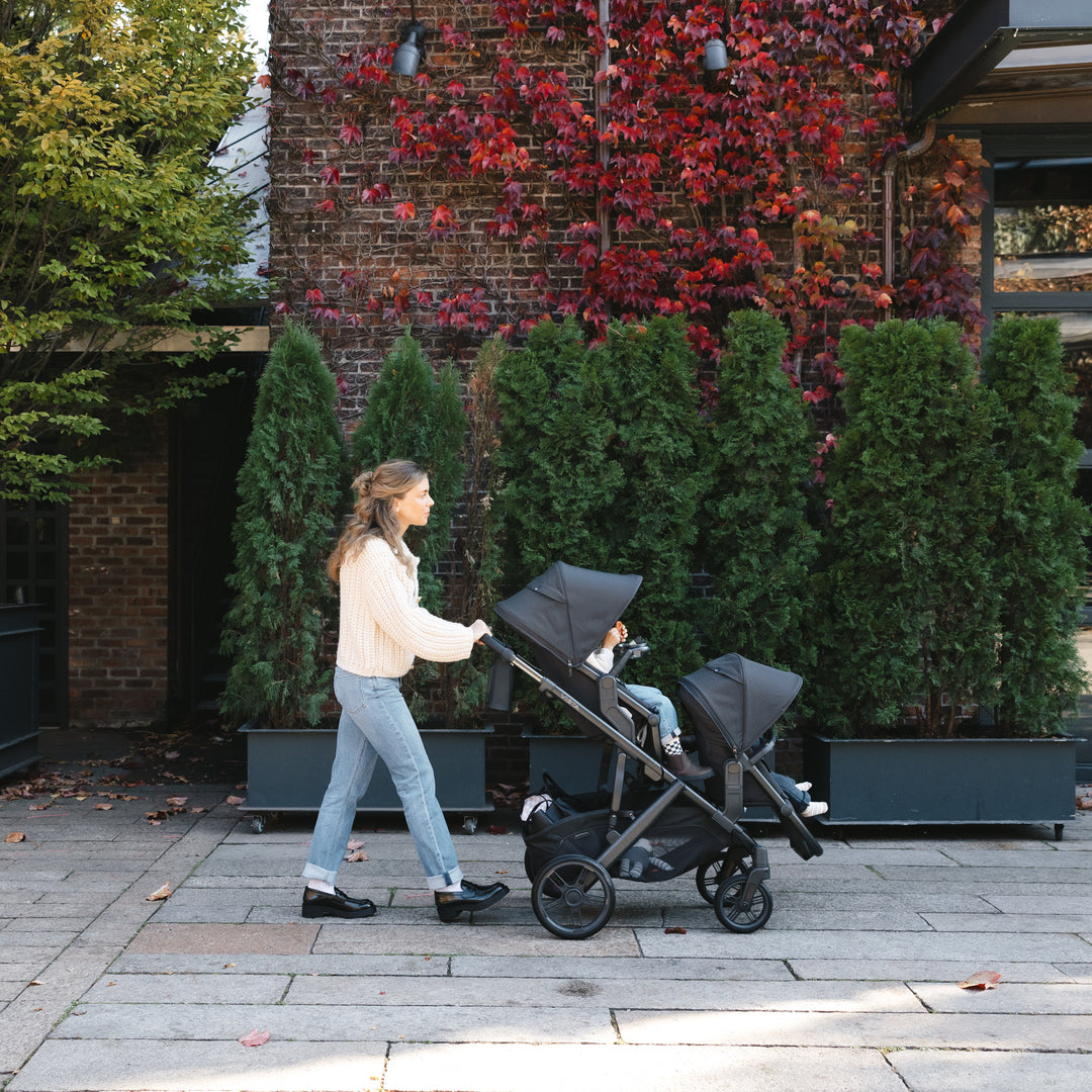 Woman pushing an uppababy vista v3 in jake with rumbleseat v3 in jake stroller with a child on a sidewalk