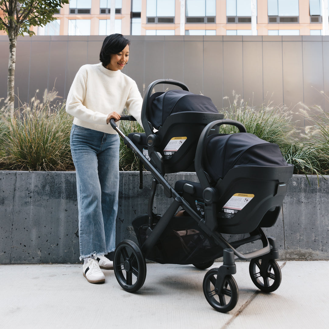 Woman pushing an uppababy vista v3 double stroller with two uppababy mesa  infant car seat