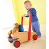 A little boy using his wagon walker to push his teddy bear.