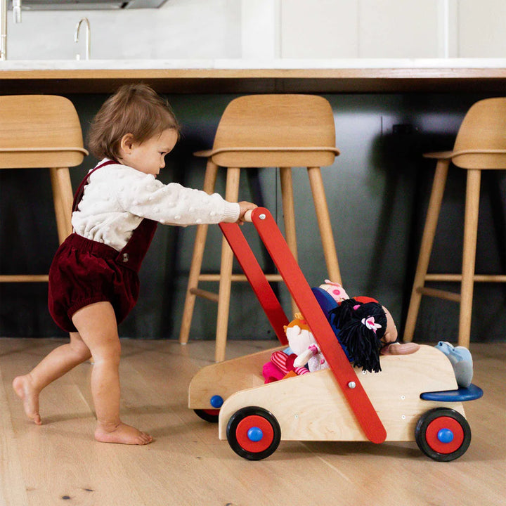 A little girl pushing her wagon walker and dolls.