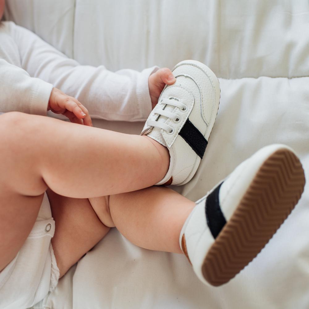 Baby holding onto a white and black little love bug co sneaker