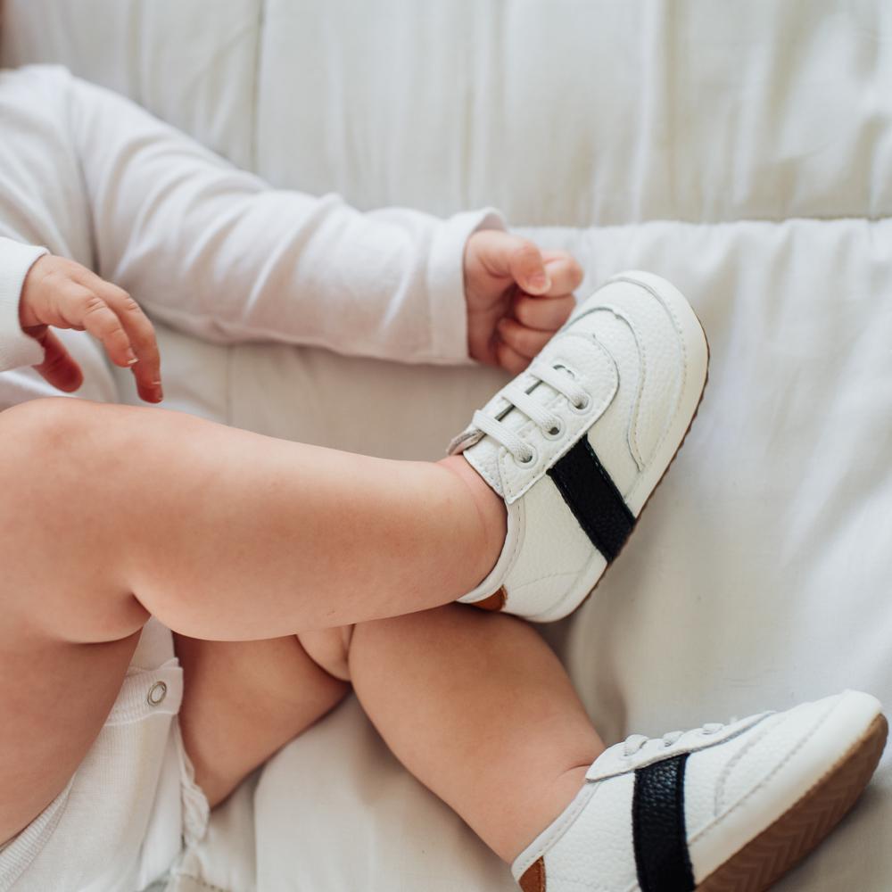 baby laying down while wearing the white and black leather little love bug sneakers