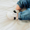 Baby sitting down, wearing the white and black Little Love Bug sneakers.