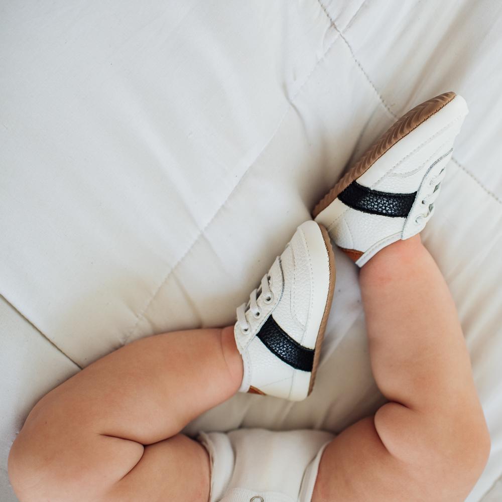 Baby wearing White and black little love bug sneakers while laying down/