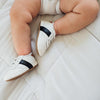 Baby laying down, wearing a pair of little love bug's white and black leather sneakers