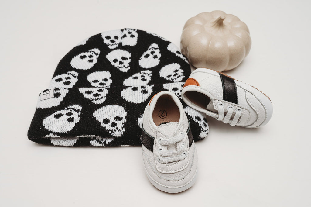 White and black little love bug sneakers next to a pumpkin.