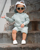 Toddler sitting while wearing a pair of white Quinn leather shoes.