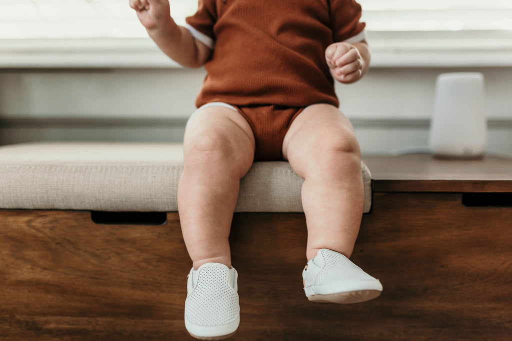 Baby wearing a pair of Little Love Bug co white leather shoes.