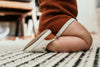 Baby sitting on ground, wearing a pair of Little Love Bug co white leather Quinn shoes.