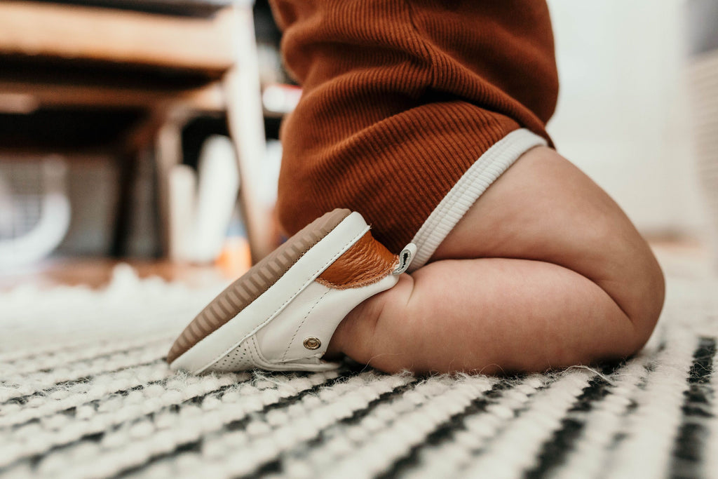 Baby sitting on ground, wearing a pair of Little Love Bug co white leather Quinn shoes.