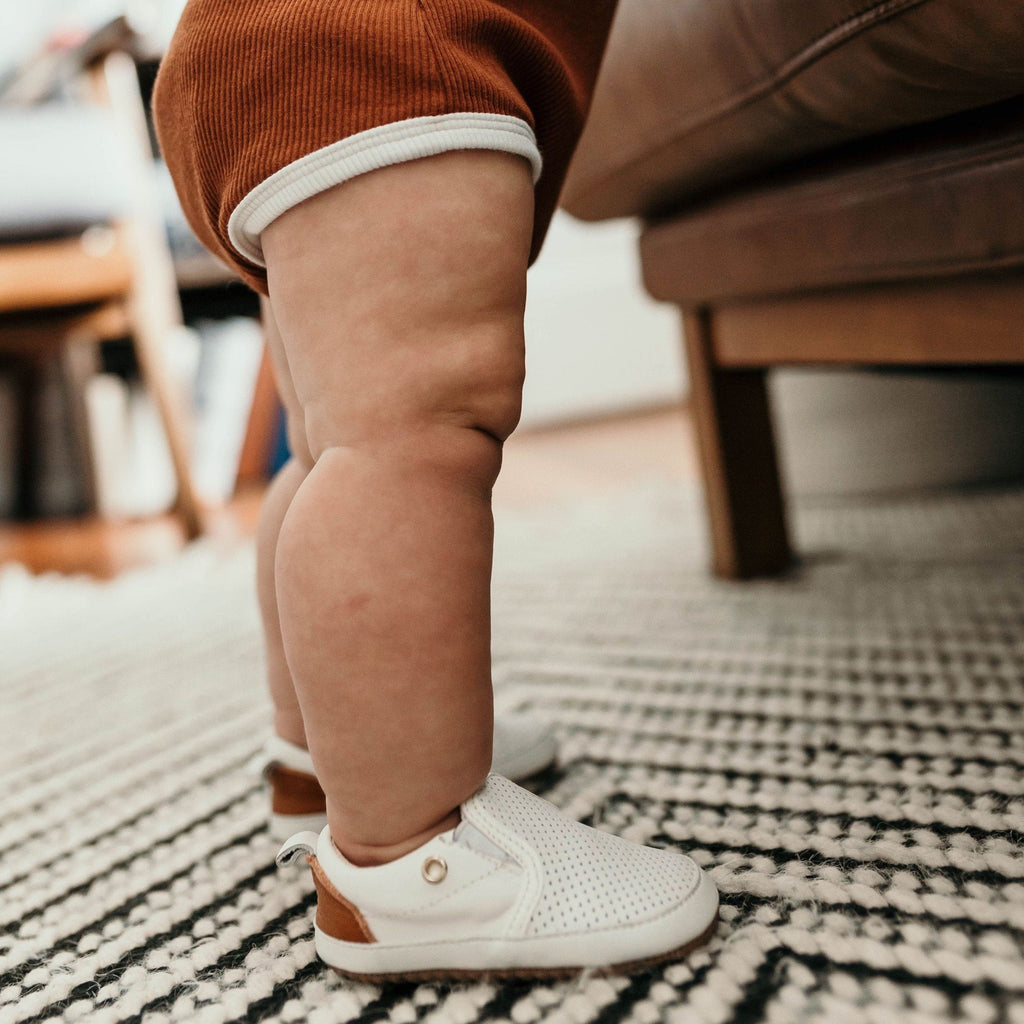 Toddler standing while wearing a pair of White Quinn Little Love Bug Co. shoes.