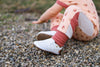 Toddler sitting on rocks while wearing a pair of white Quinn leather shoes, made by Little Love Bug Co.