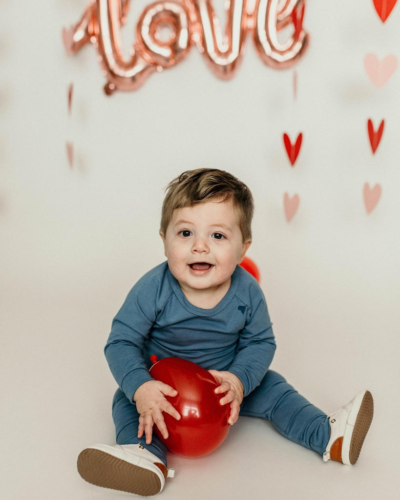 Baby sitting down, wearing a pair of Little Love bug Co white leather Quinn shoes.