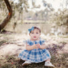 Baby sitting in grass in a pair of  Little Love Bug Co. white t-bar shoes.