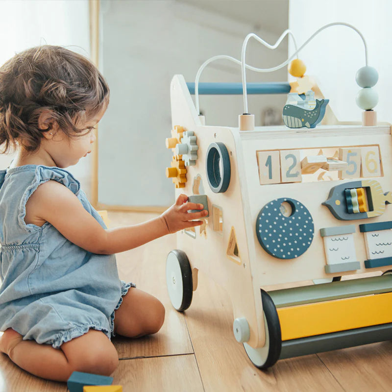 Toddler seated playing with Wonder & Wise Busy Busy Baby Walker, wooden educational push toy for fine motor skill development