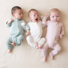 Three babies wearing the Kyte Zipper Romper in shades Cloud, Blush, and Sage.