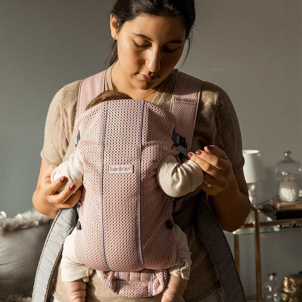mom facing forward comforting baby in babybjorb mini baby carrier pink
