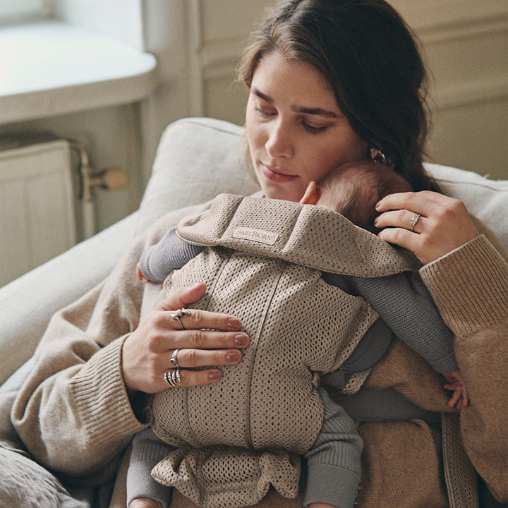 mom comforting baby in mini baby carrier by babybjorn grey beige mesh