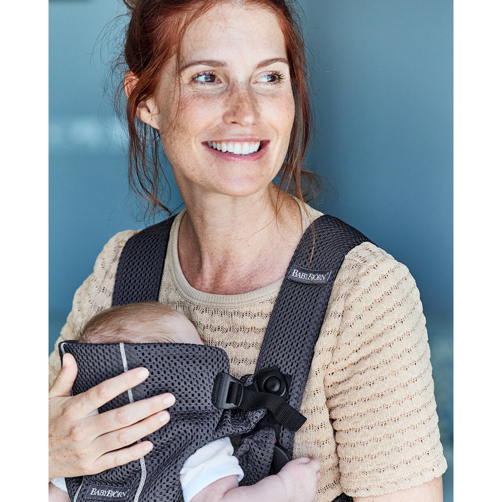 mom smiling facing forward with baby in babybjorn baby carrier mini