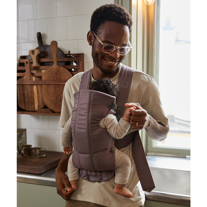 father smiling in kitchen with baby in babybjorn dark purple mini baby carrier