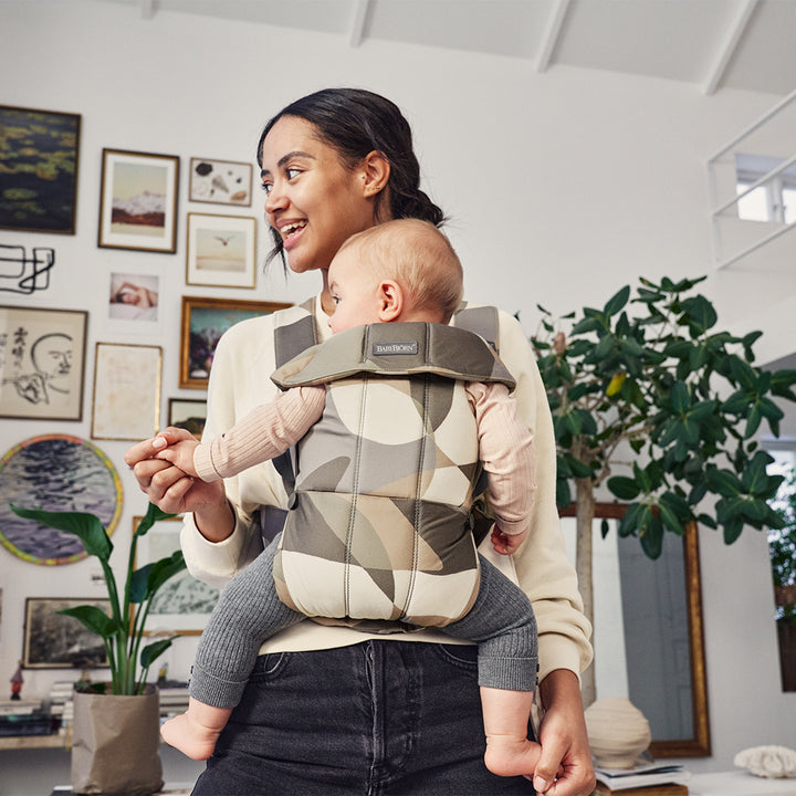 mom smiling in living area with infant in babybjorn khaki green baby carrier