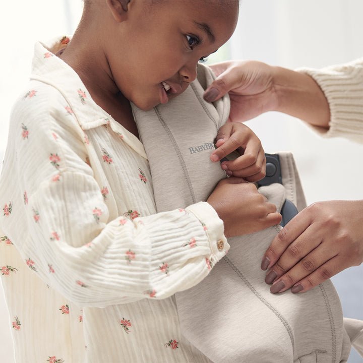 baby holding babybjorn infant mini baby carrier in light beige