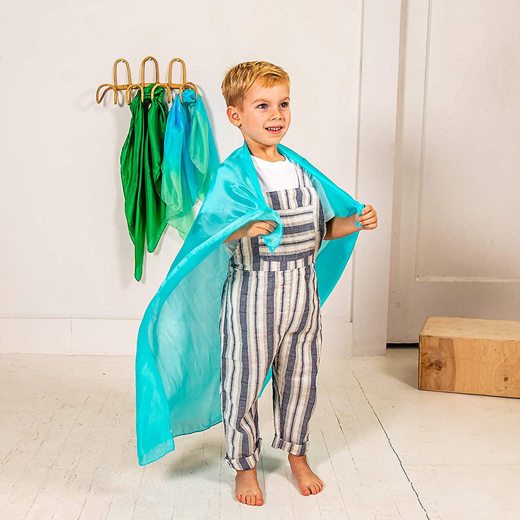 Lifestyle image of child using a turquoise Playsilk as a to cape. 