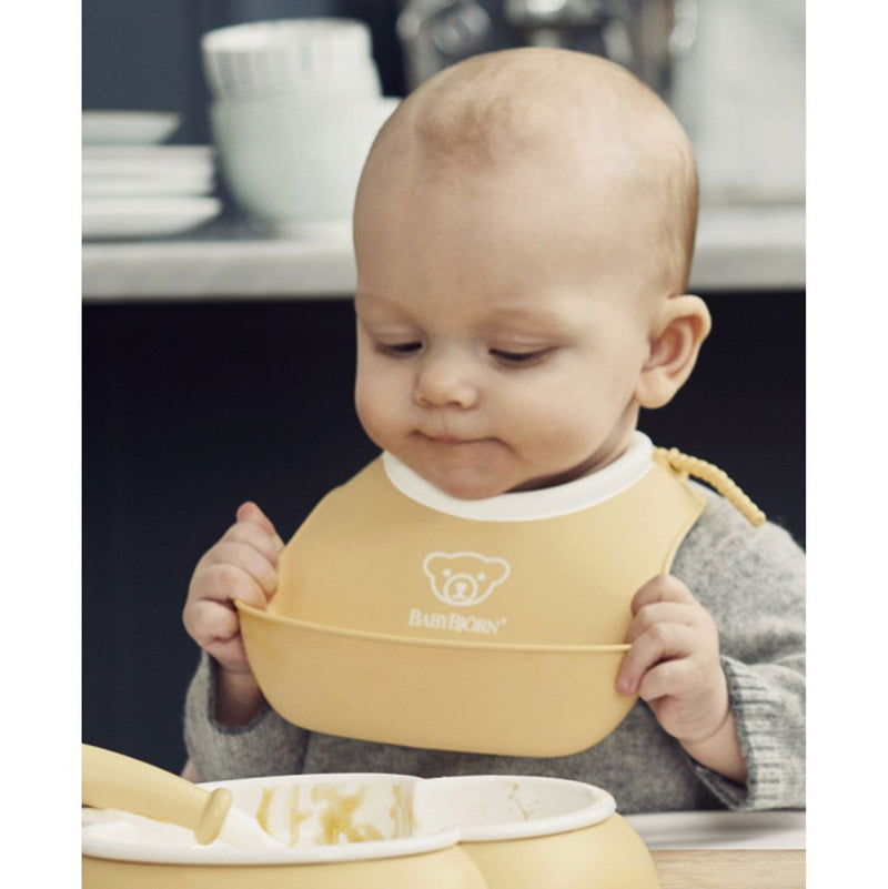 Baby Using Babybjorn Soft Feeding Bib Set in Yellow, making mealtime cleanup simple