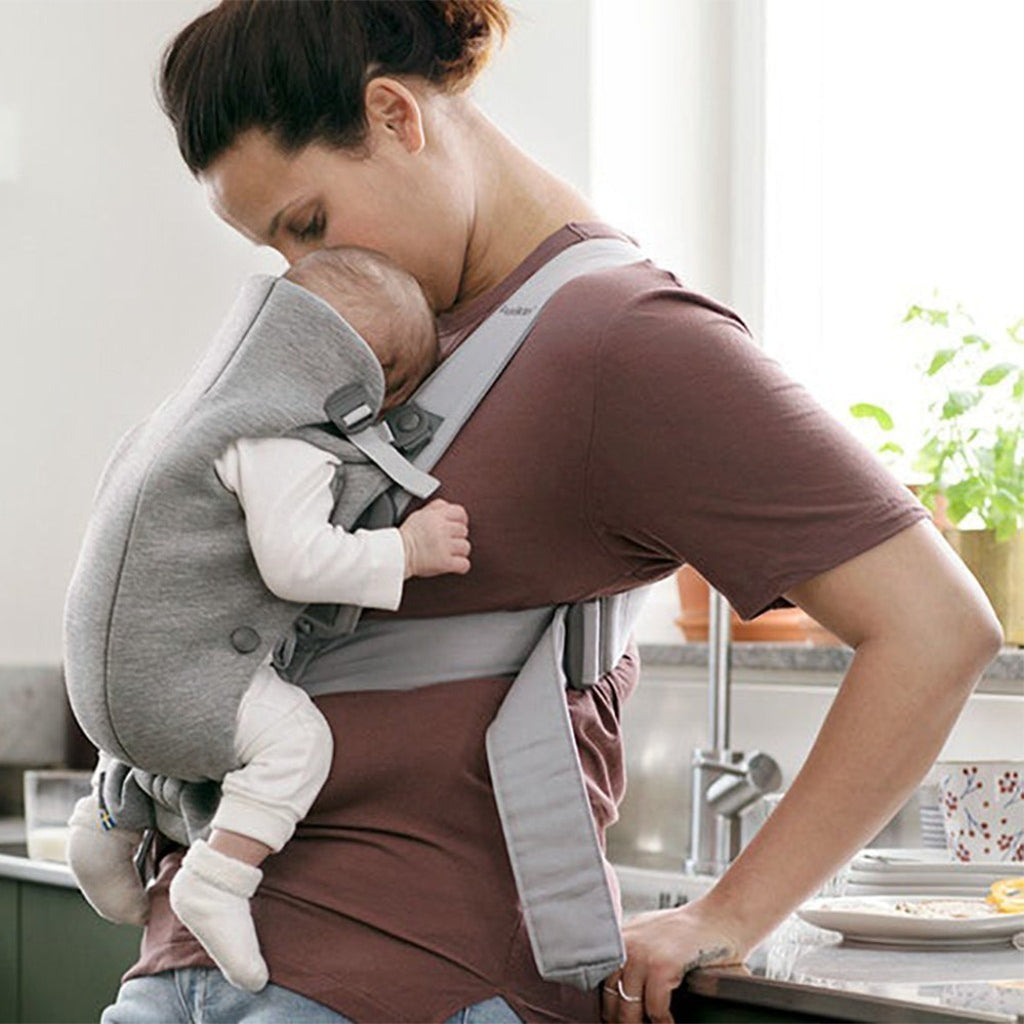 mom leaning against counter wearing babybjorn cotton baby carrier mini