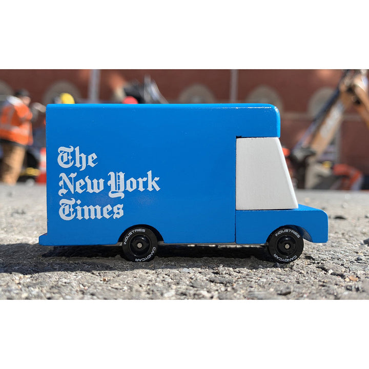 A Candylab Toys New York Times wooden blue van parked on the sidewalk, part of a child's imaginative world.