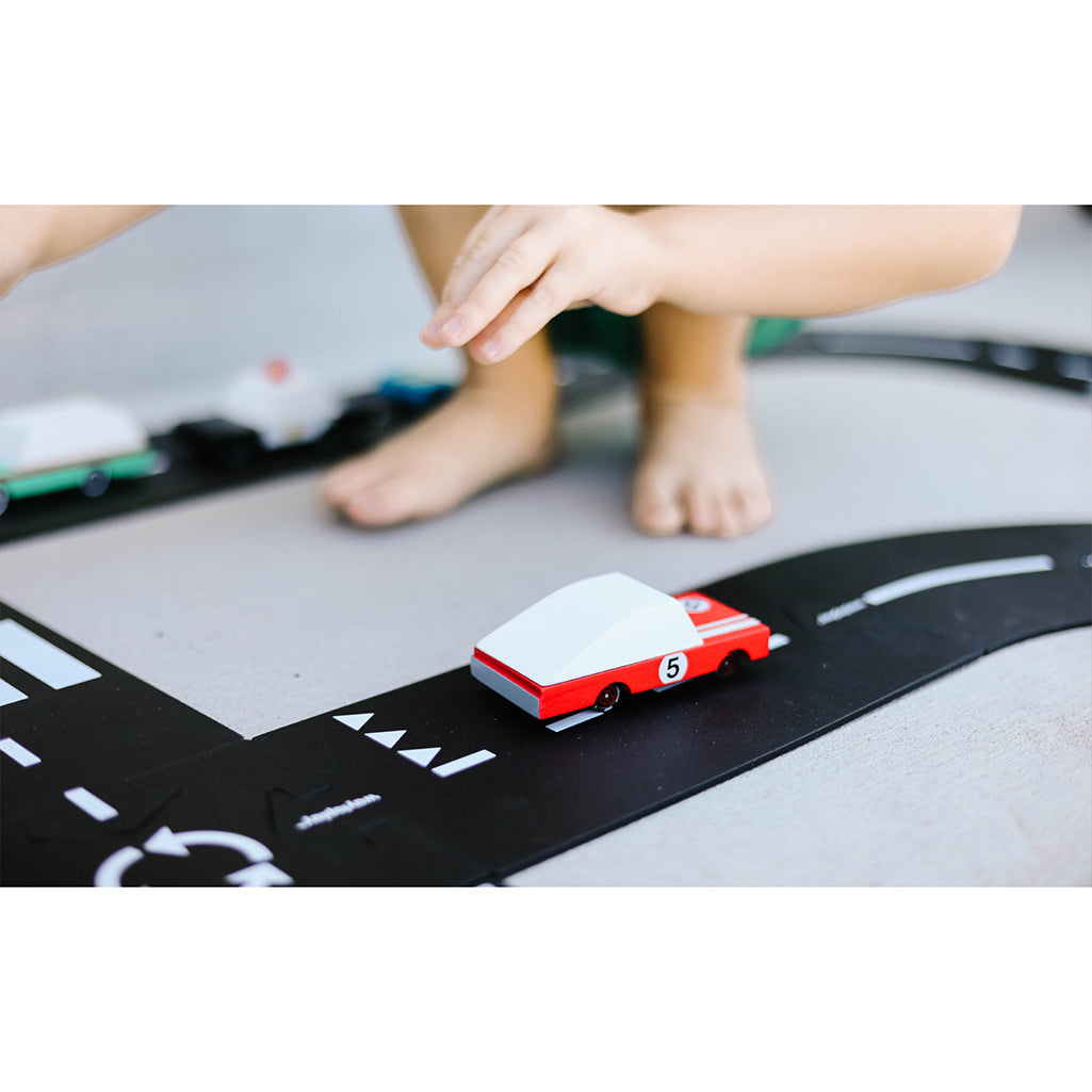 A child playing with the Candylab Toys Red Racer #5 wooden car, participating in a pretend race.