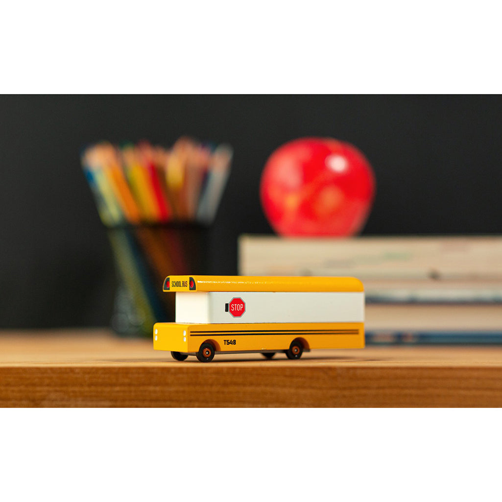 A Candylab Toys wooden yellow school bus sitting on a desk, ready for children to engage in imaginative play.