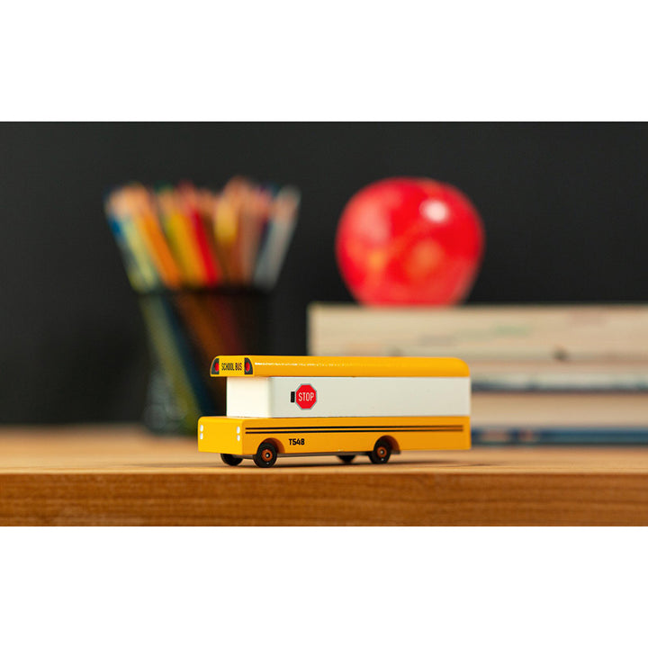 A Candylab Toys wooden yellow school bus sitting on a desk, ready for children to engage in imaginative play.