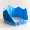 Sarah's Silk Star Silk Crown Children's Pretend Dress-Up Crown. Bright Blue silk crown with light blue band around the bottom. Golden starts and dots spattered all around the bright blue portion. Elastic band around the back. Side view showing the elastic band.