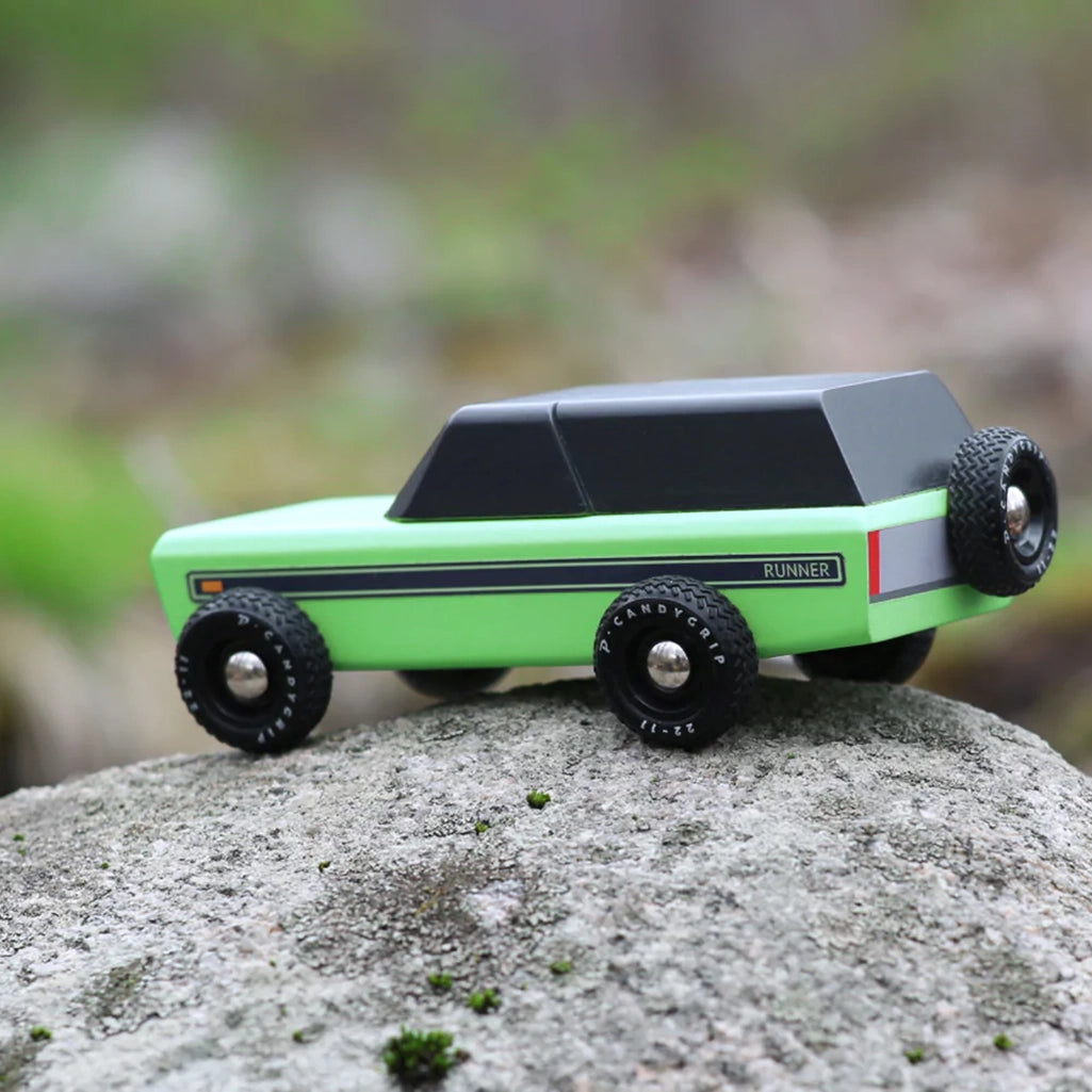 A Candylab Runner vintage children's wooden toy vehicle resting outside on a rock, showing off its outdoor appeal.